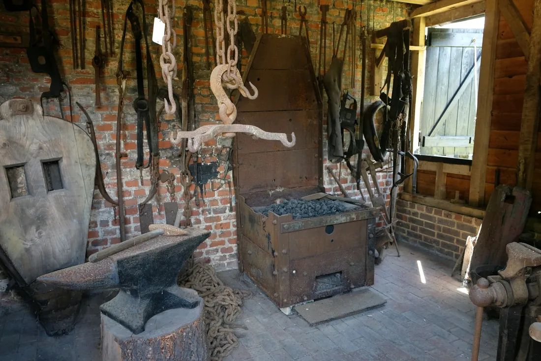 Interior de una herrería con fragua, yunque sobre cepo de madera y herramientas de forja colgadas en la pared
